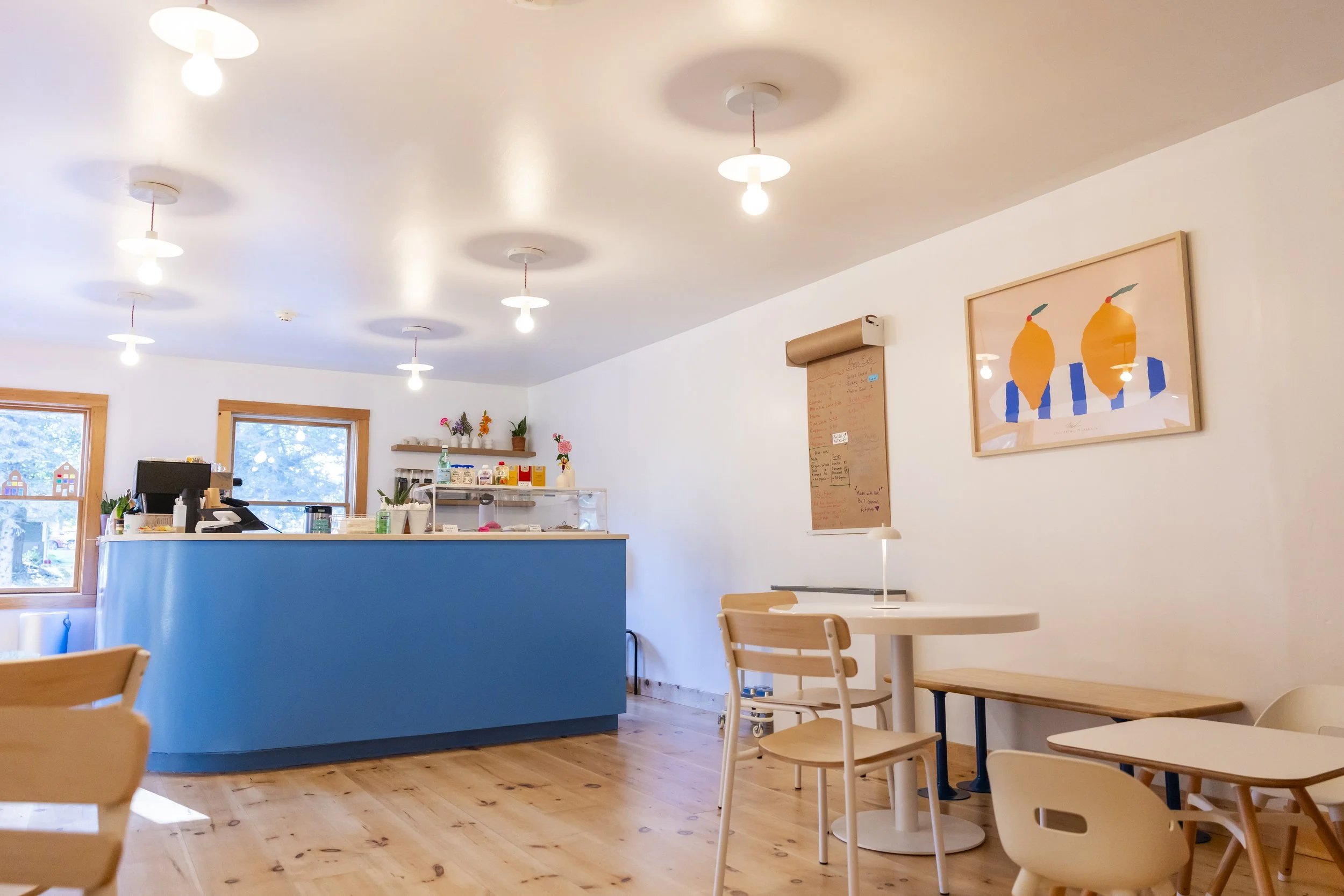 A cozy cafe interior with wooden furniture, white walls, a blue counter, and colorful artwork on the wall.