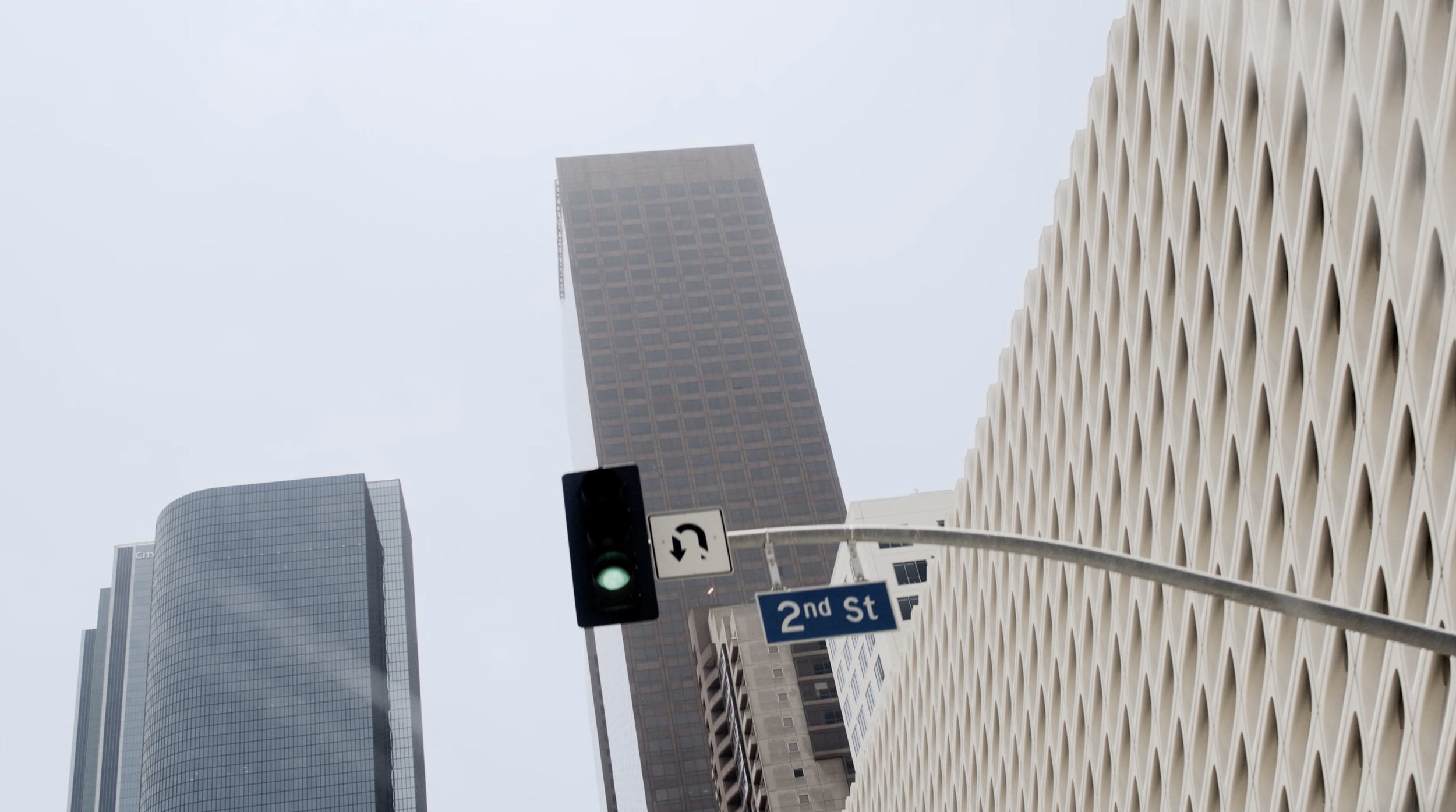 Cityscape with tall buildings, traffic light showing green, and a street sign indicating 2nd Street. The buildings vary in architectural style and height, with one building having a honeycomb-like facade.