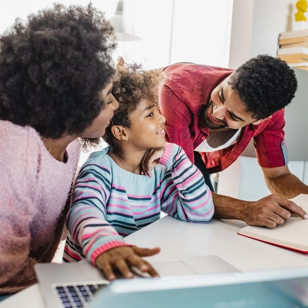 Parents sitting with their young daughter at a desk supporting her with learning during a family parenting counseling session.