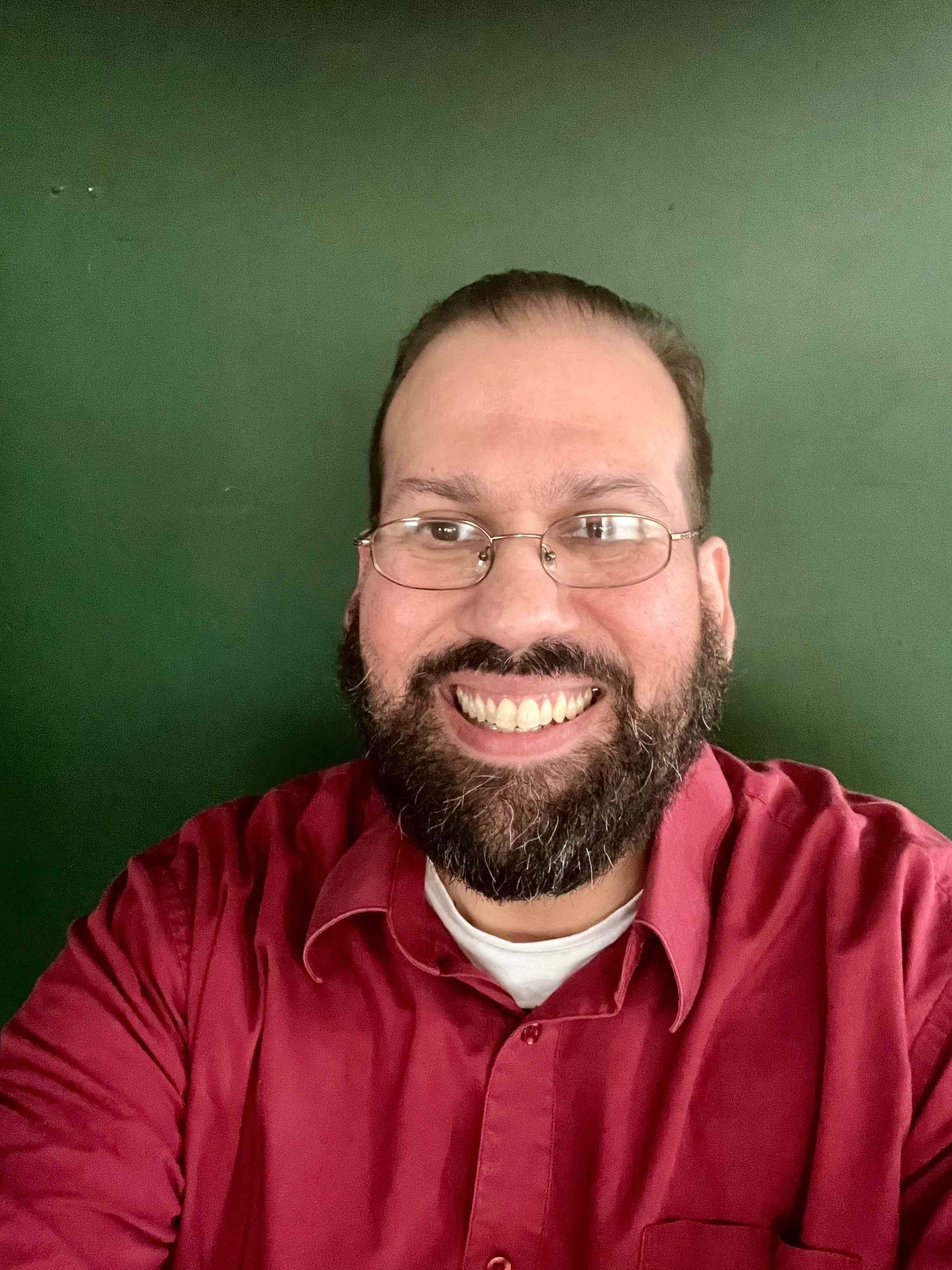 Man with red shirt and glasses smiling in front of green wall