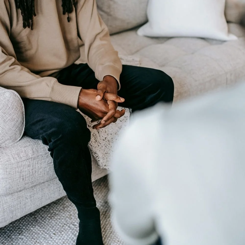 Person sitting on a couch with hands clasped during an EMDR therapy session focused on trauma and anxiety treatment.