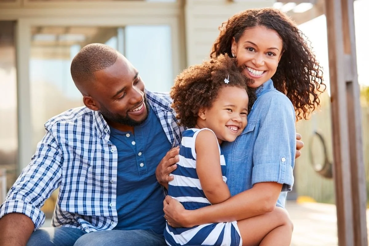 Smiling parents hugging their young daughter outdoors during a family therapy context.