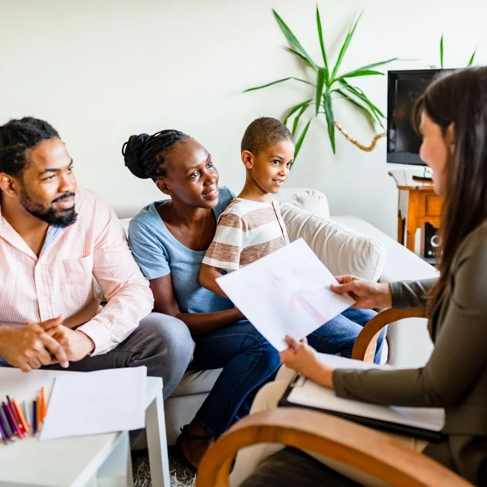 Family sitting on a couch during a parenting counseling session as a therapist reviews the child's drawing