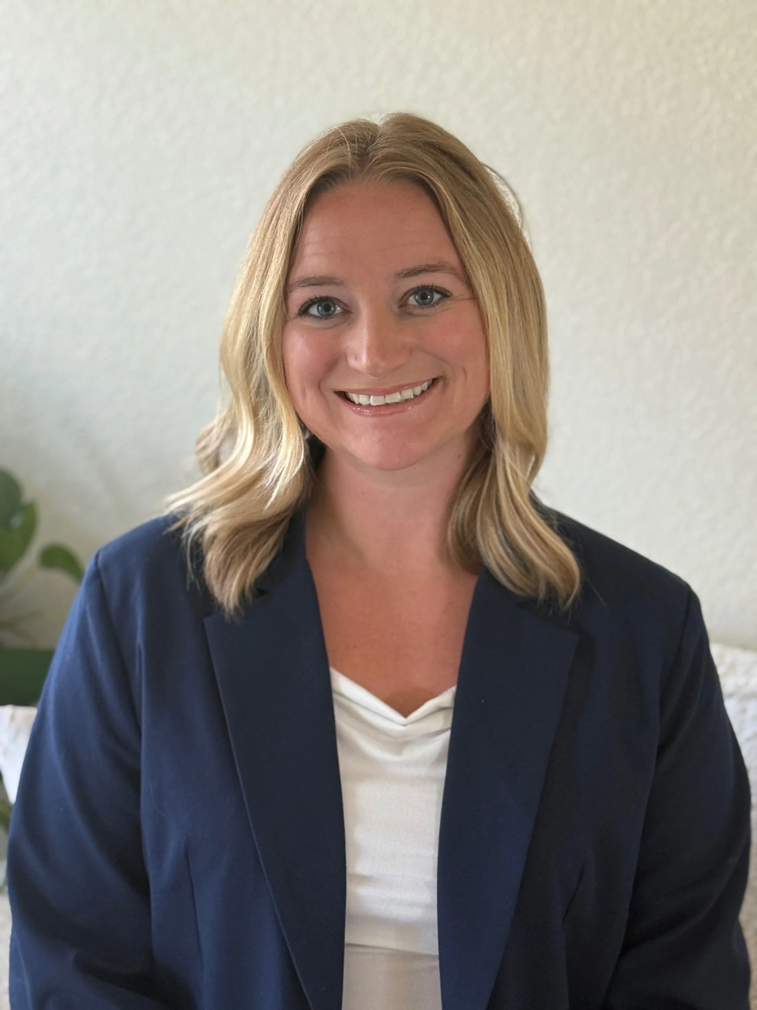 Woman with blonde hair smiling in a white shirt and blue blazer