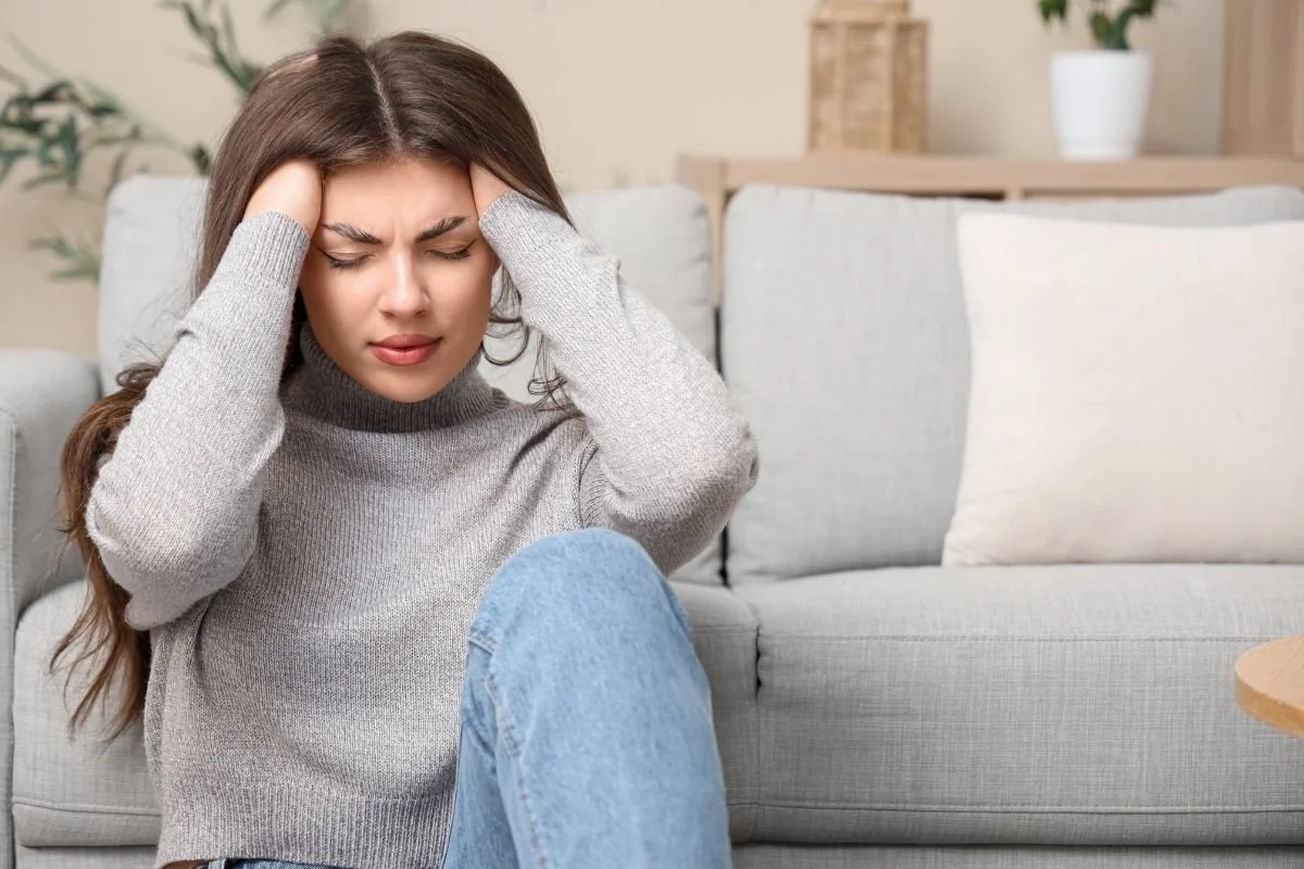 Woman sitting on the living room floor with eyes closed and hands on her head coping with stress and a panic attack.