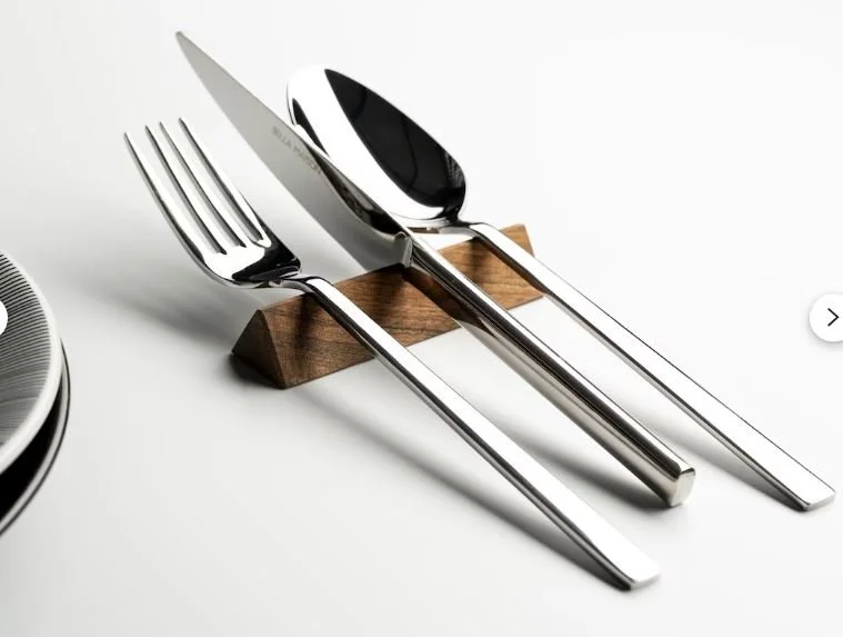 A set of silver cutlery including a fork, a knife, and a spoon resting on a wooden holder, placed on a white surface.