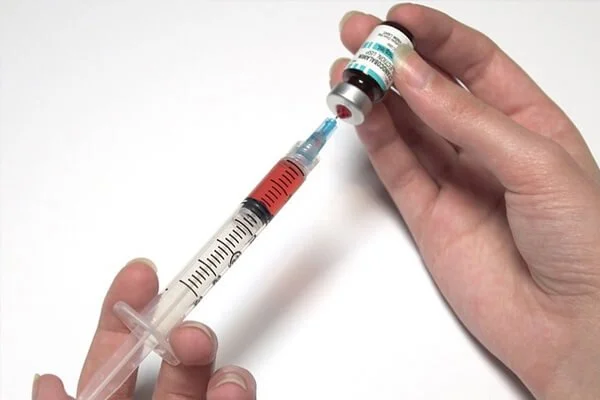 A person drawing a vitamin shot into a syringe from a small vitamin vial.