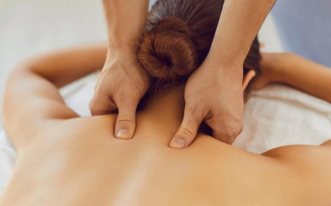 Massage therapist giving a back massage to a woman with red hair in a bun.