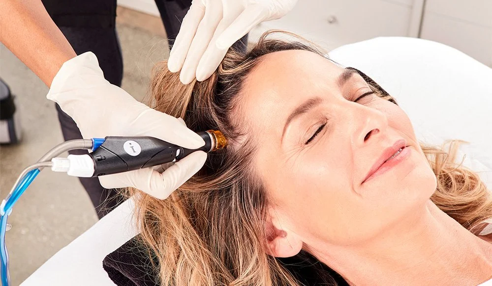Woman receiving a cosmetic laser treatment on her scalp from a medical professional wearing gloves.