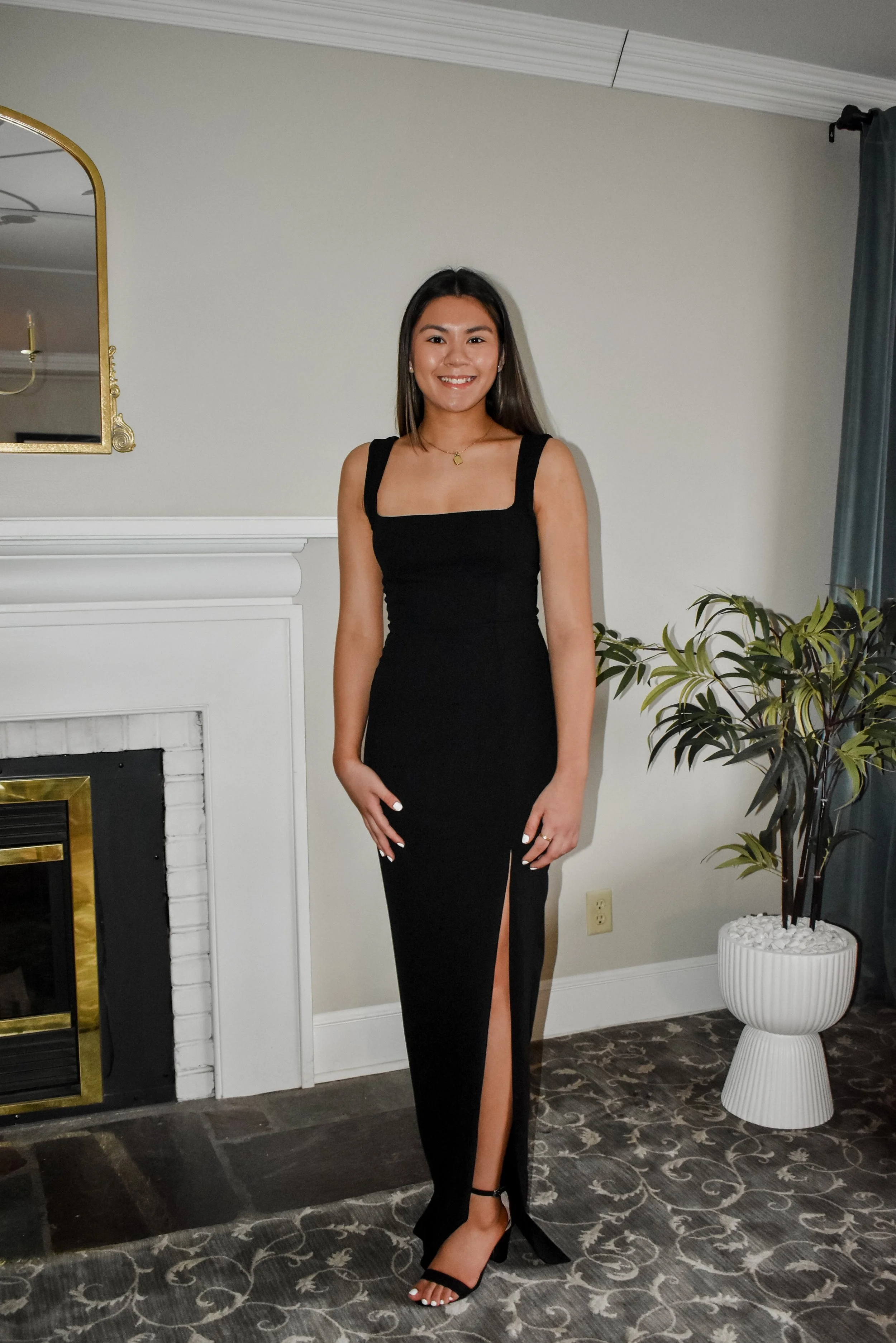 image displays Chloe Pennoni in a long black dress with black heels in front of a fireplace