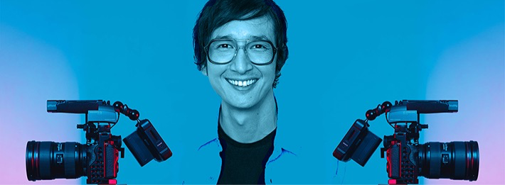 Person smiling with two professional video cameras against a blue background.