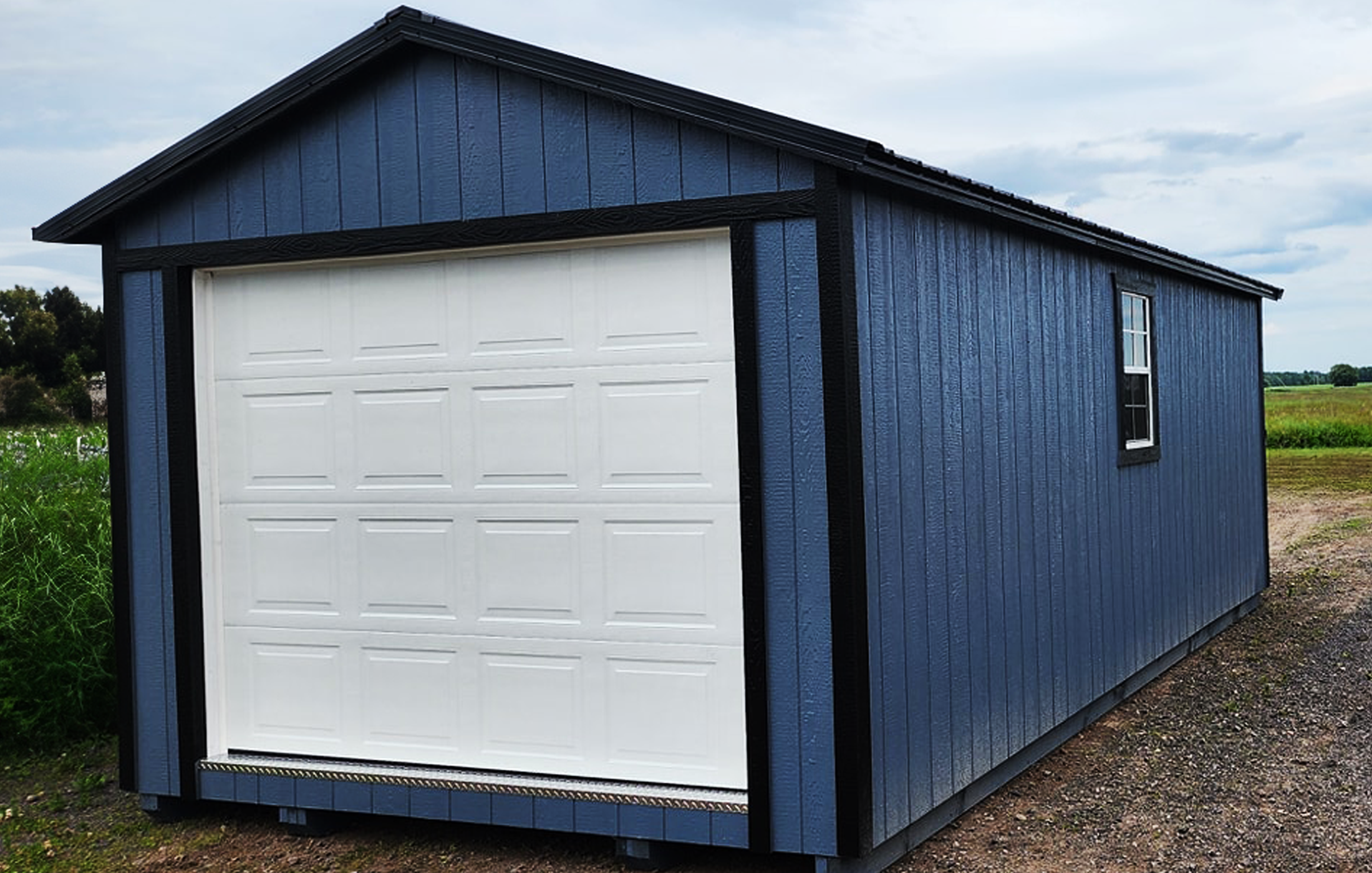 Cabanons nature, cabanon Outaouais. Garage en bois peint en bleu avec porte de garage blanche et petite fenêtre à droite, situé dans un espace rural.