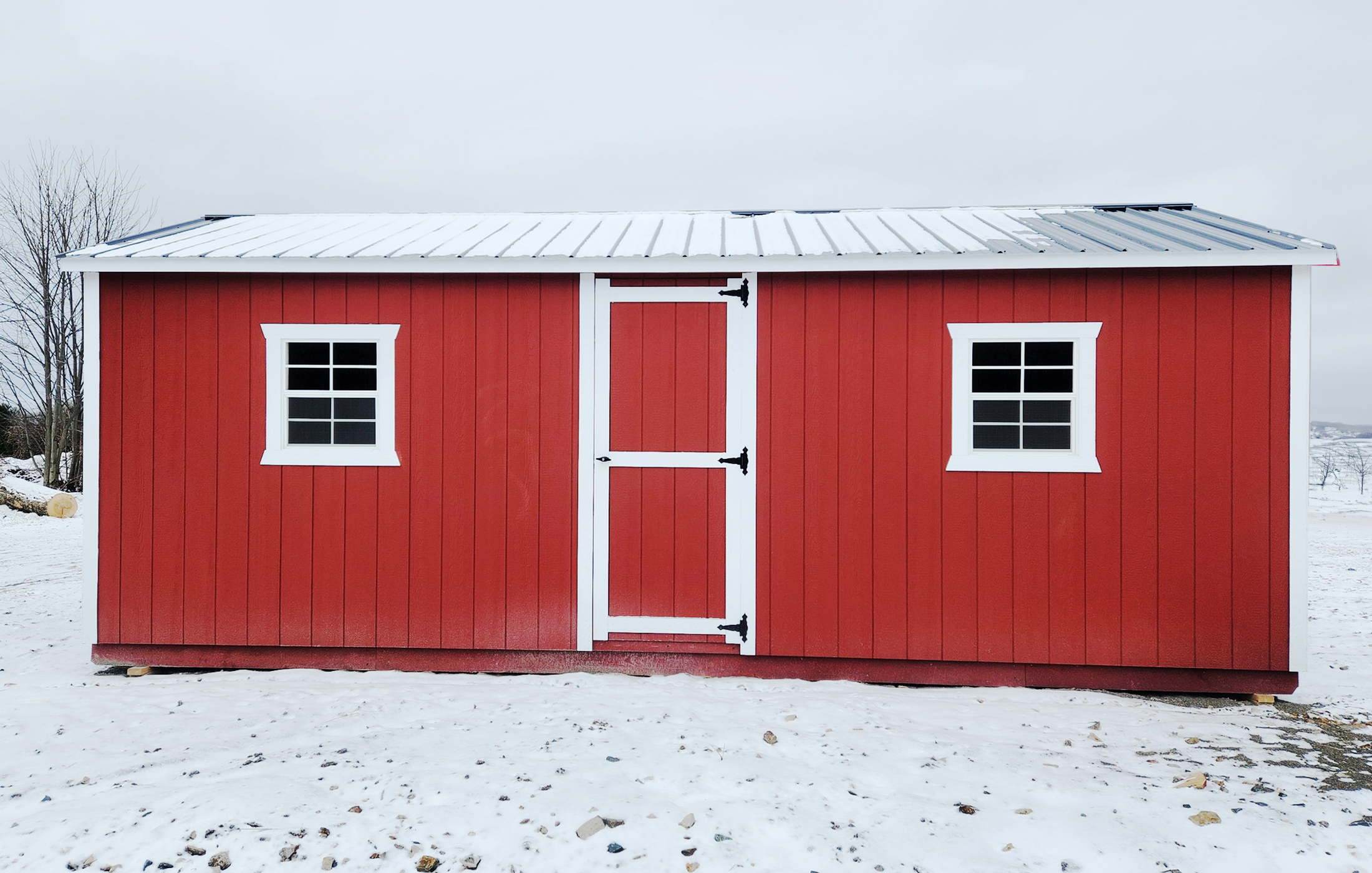 Cabanons nature, cabanon Outaouais. Petite cabane rouge en bois avec deux fenêtres à petits carreaux et un toit en métal, dans un paysage enneigé. Cabanon. Backyard Shed. Remise. Cabanons.