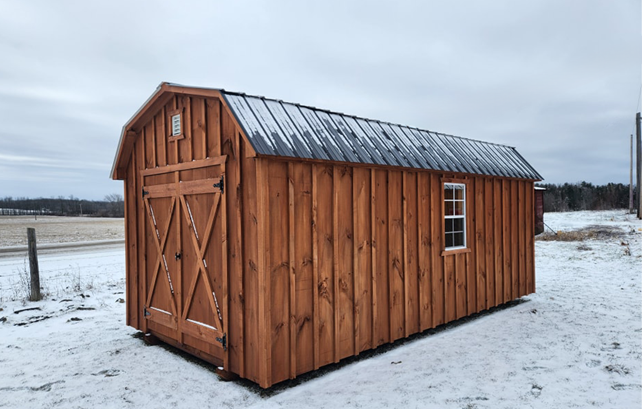 Cabanons nature, cabanon Outaouais. Abri en bois avec un toit en métal, situé dans un paysage enneigé, sous un ciel gris, avec un petit fenêtre et double porte en bois. Cabanon. Backyard Shed. Remise. Cabanons.