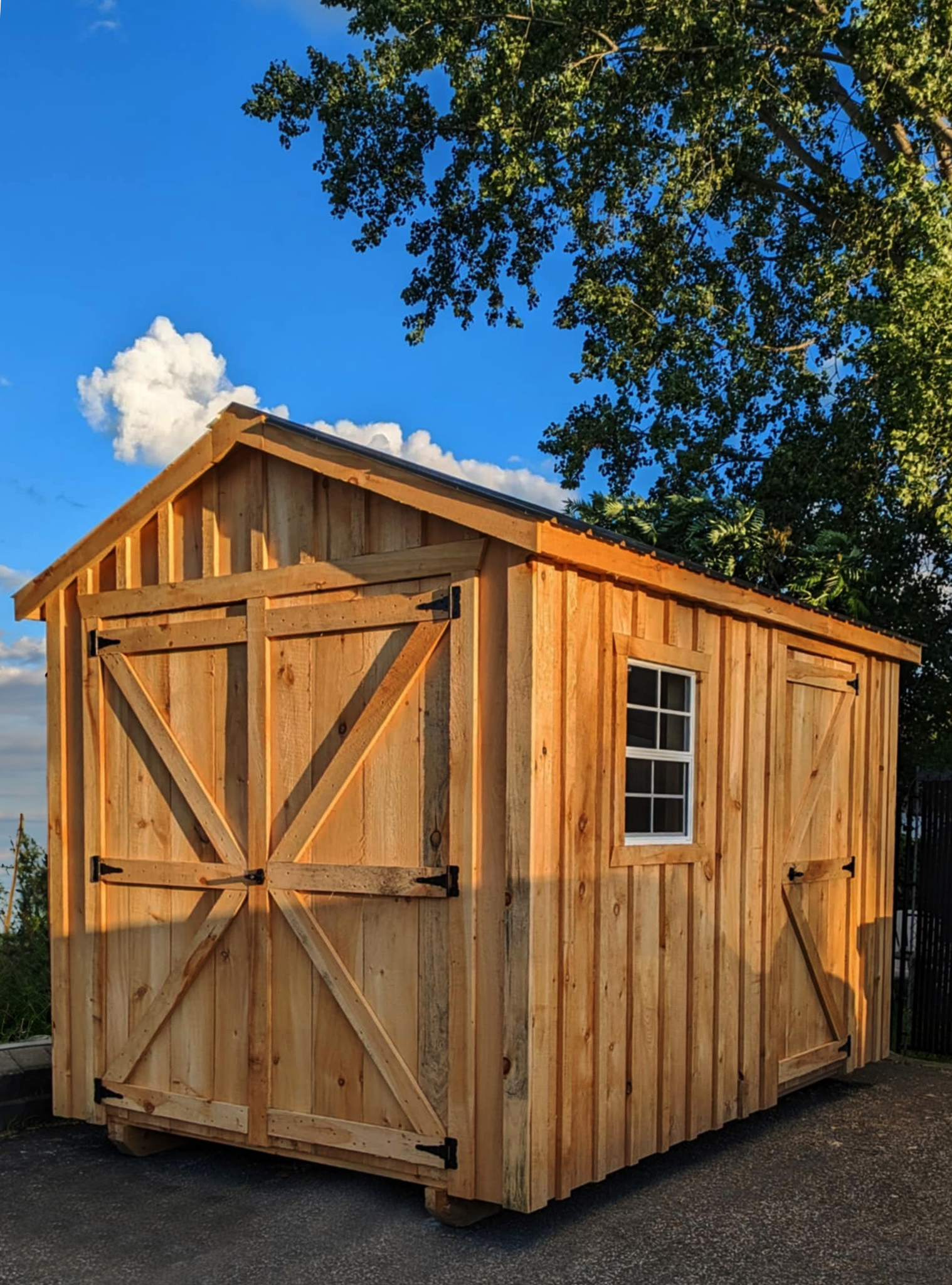 Cabanon Outaouais, Cabanons Outouais. Une petite cabane en bois avec fenêtres, construite en bois clair, sous un ciel bleu avec des nuages et entourée d'arbres verts. Cabanon. Backyard Shed. Remise. Cabanons.