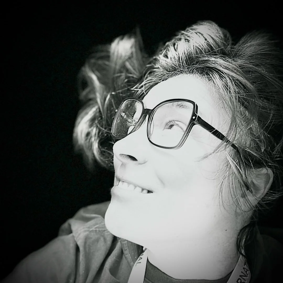 Portrait d'une femme souriante portant des lunettes, en noir et blanc.