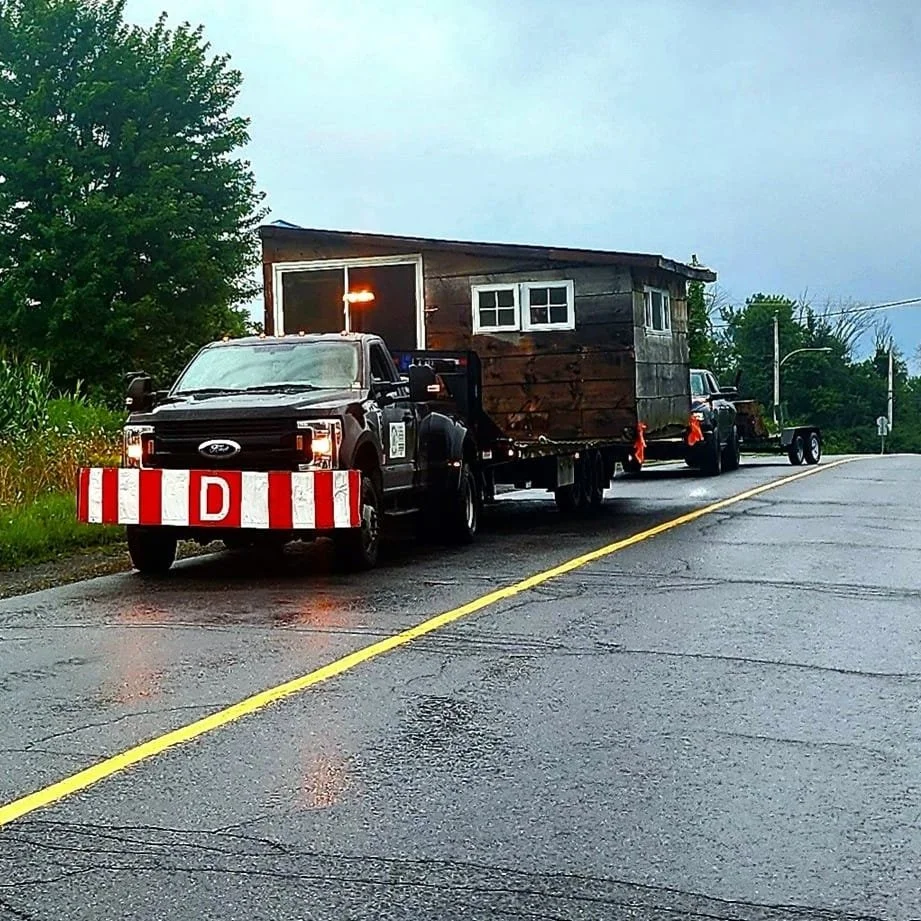 Cabanon Outaouais, Cabanons Outouais. Camion avec une maison en bois montée dessus, sur une route mouillée