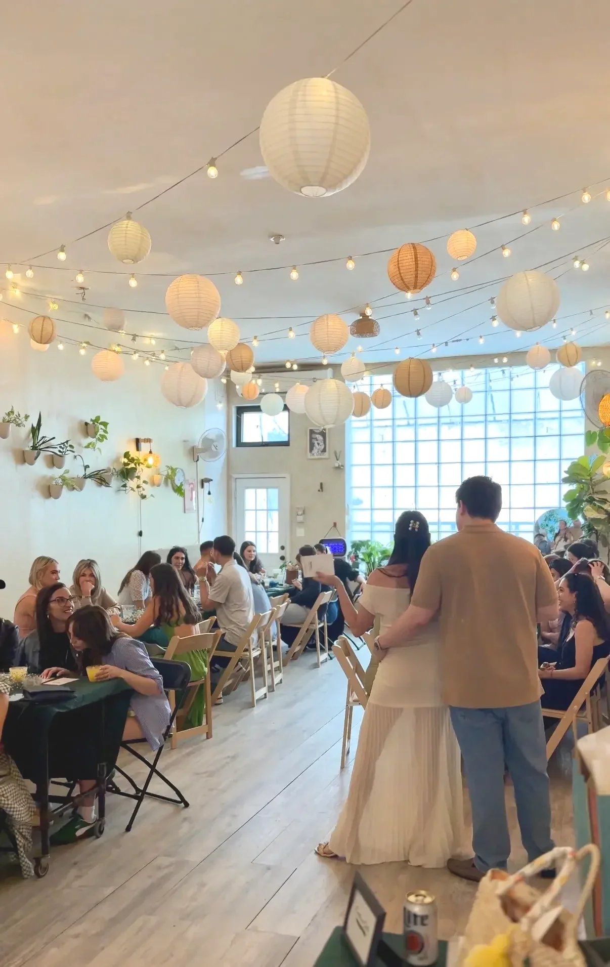 Baby shower guests mingling under paper lanterns and string lights at Bat Haus, a Brooklyn baby shower venue.