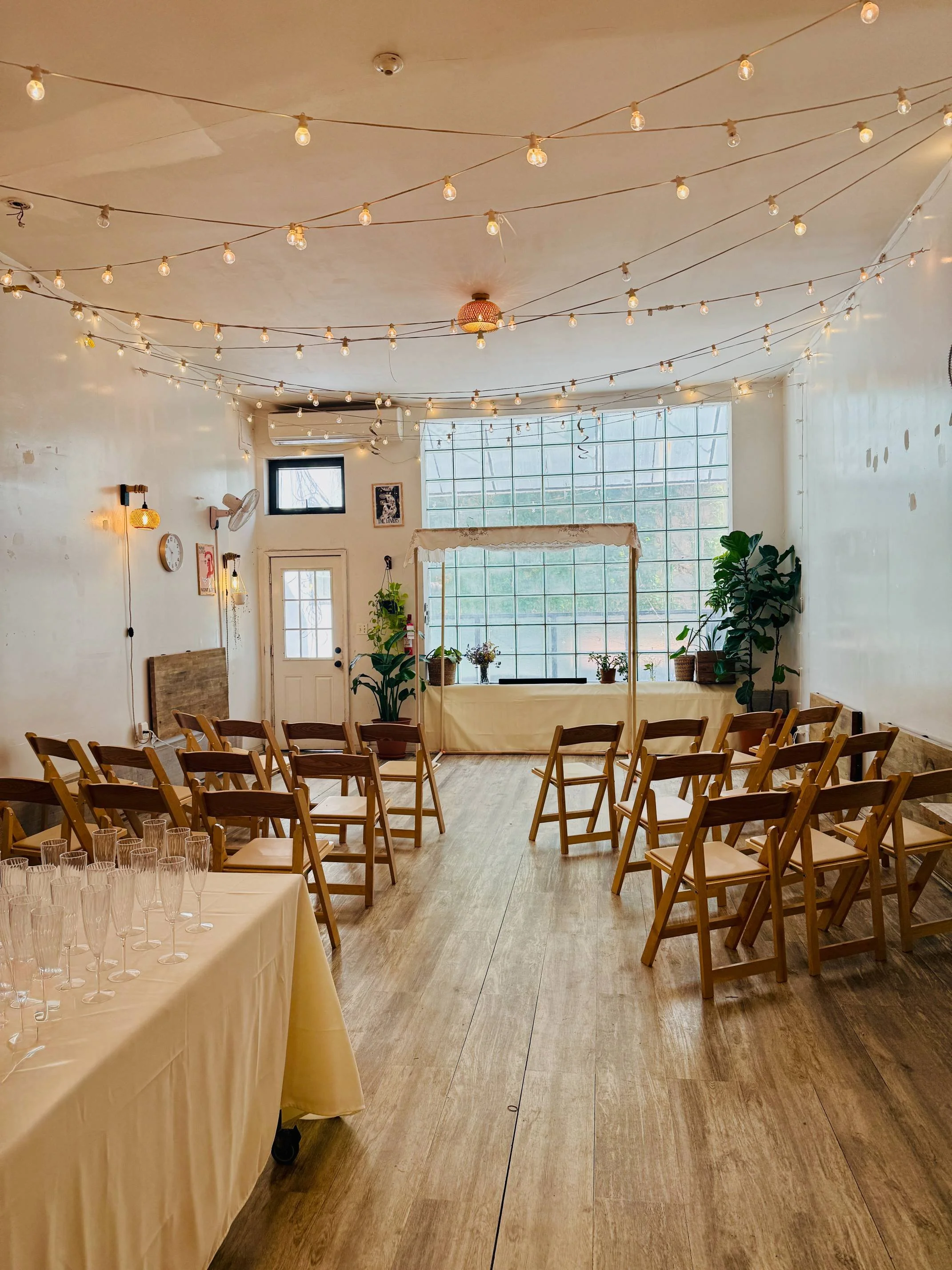 Jewish wedding chuppah ceremony setup at Bat Haus Brooklyn event space with wooden chairs and glass block window backdrop in Williamsburg NYC