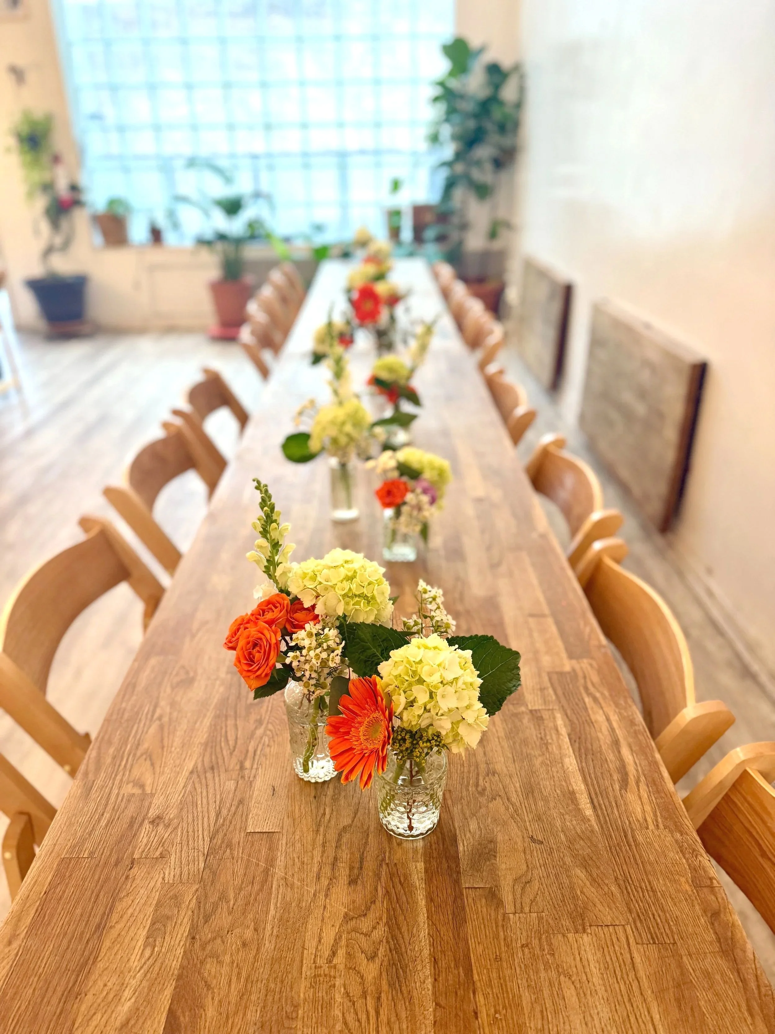 Long wooden table at Bat Haus styled with seasonal bud vase floral arrangements as part of the Styled Package, featuring bright blooms, greenery, and a warm, ready-to-host event setup in Brooklyn.