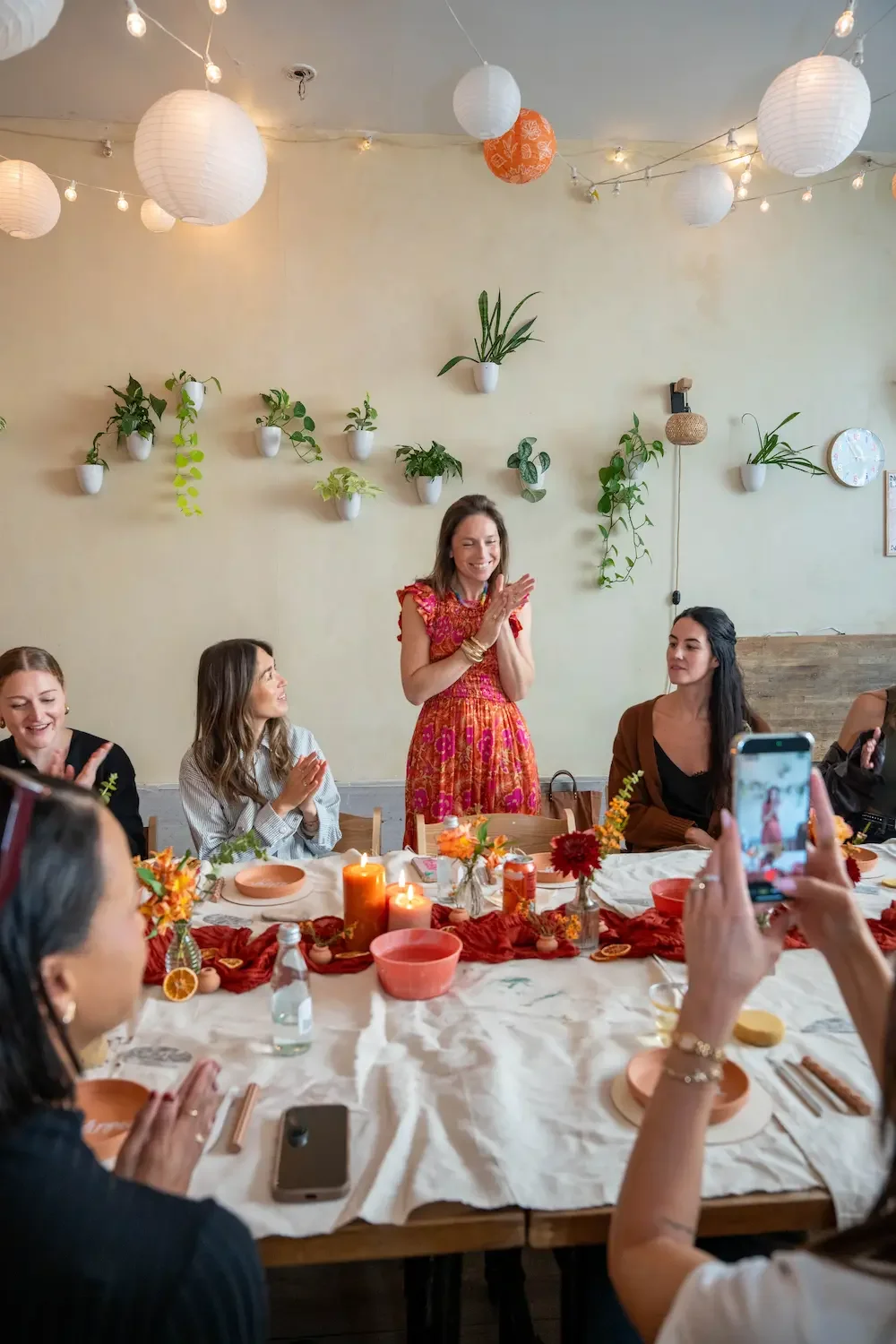 Host welcoming about 20 creators to a brand activation pottery workshop at Bat Haus in Brooklyn, with guests seated around a candlelit table of clay pieces and autumn flowers