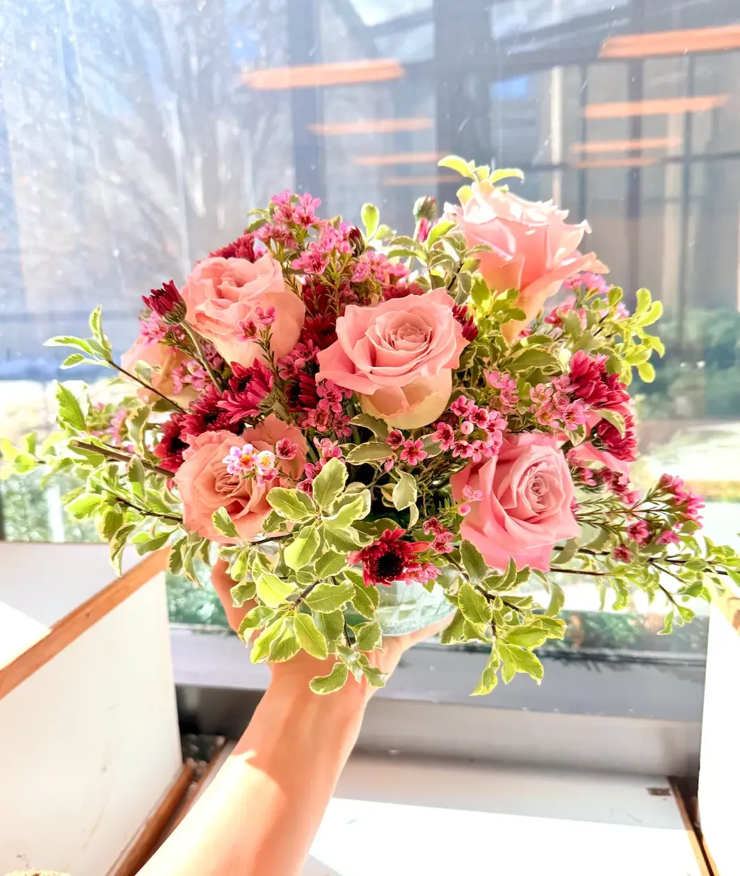 Bud vase floral add-on at Bat Haus in Brooklyn featuring pink roses and seasonal blooms arranged in a glass vase near a sunlit window in a Williamsburg event space.