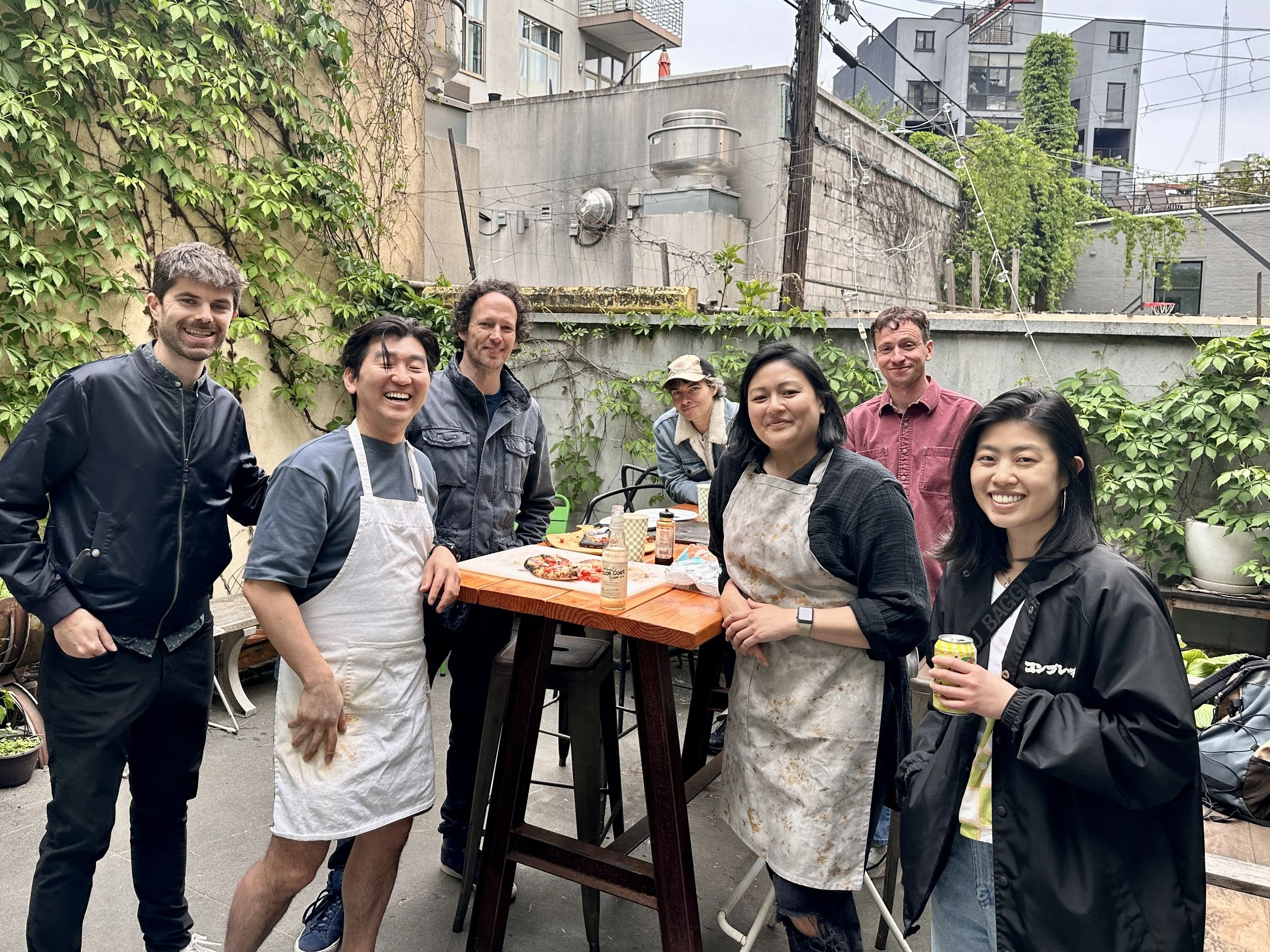 Guests enjoying a casual community gathering in the Bat Haus backyard in Brooklyn, part of the Essential Package, featuring shared tables, natural light, greenery, and an intimate outdoor atmosphere.