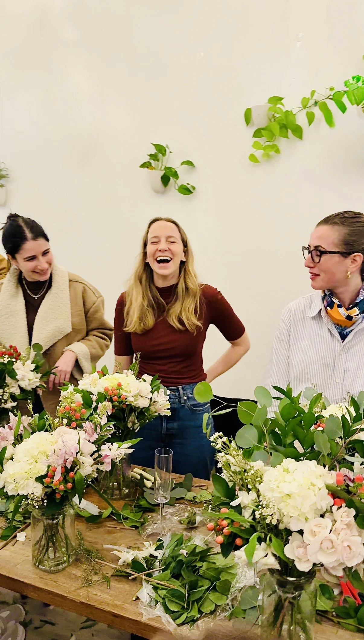 Guests laughing during a birthday floral workshop at Bat Haus in Williamsburg Brooklyn, private party experience with seasonal flower arrangements and greenery.