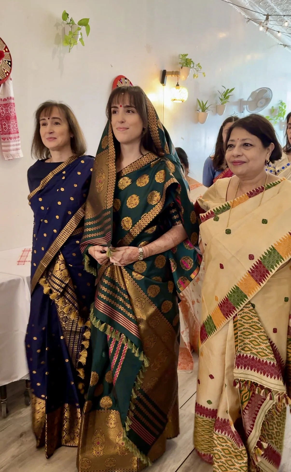 Women dressed in traditional South Asian attire during a cultural celebration ceremony at Bat Haus in Brooklyn, wearing vibrant saris with gold detailing.
