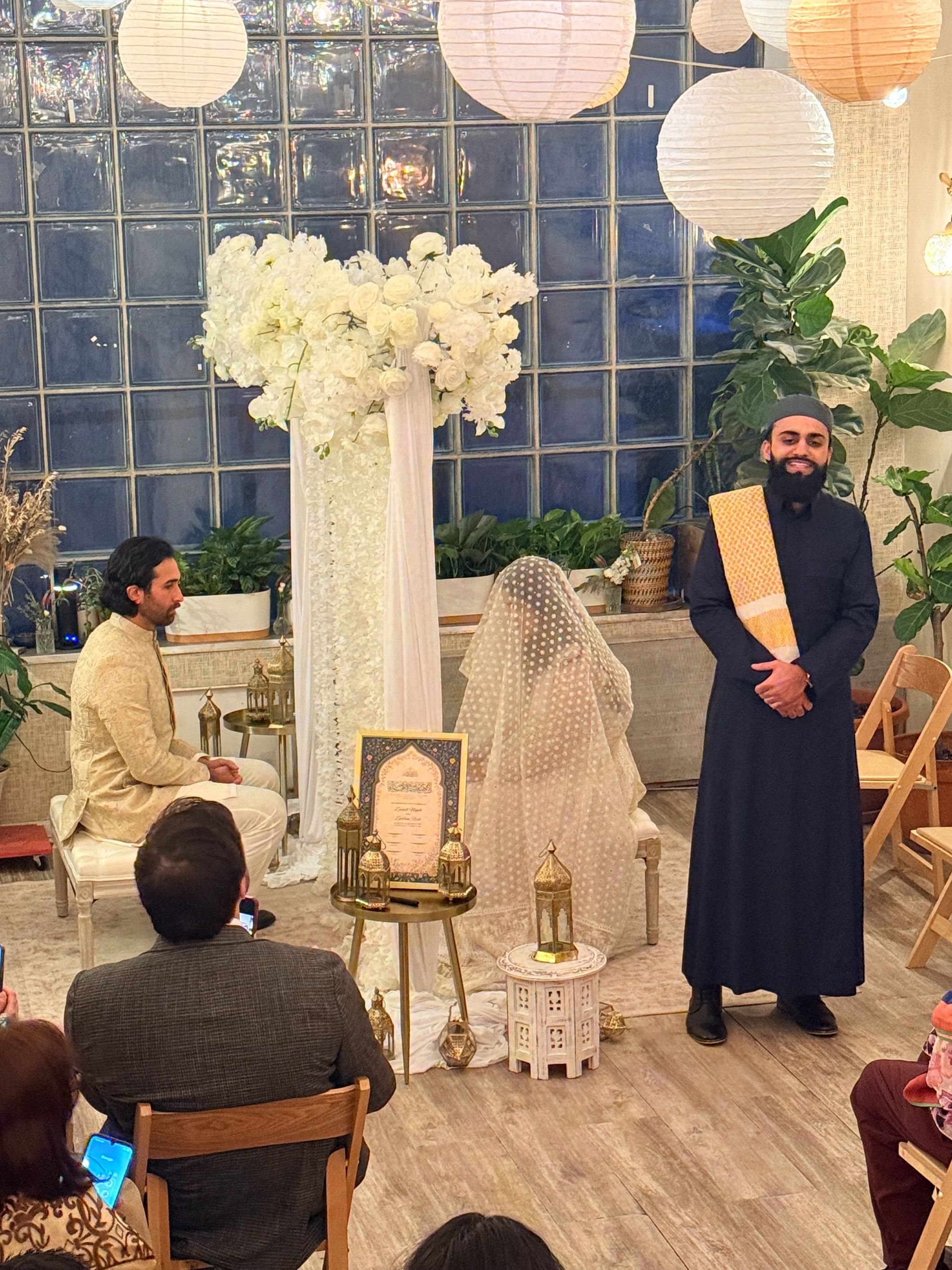 Intimate nikah wedding ceremony at Bat Haus in Brooklyn, featuring the bride and groom seated beneath a floral arch with traditional Islamic decor and lanterns in a sunlit event space.