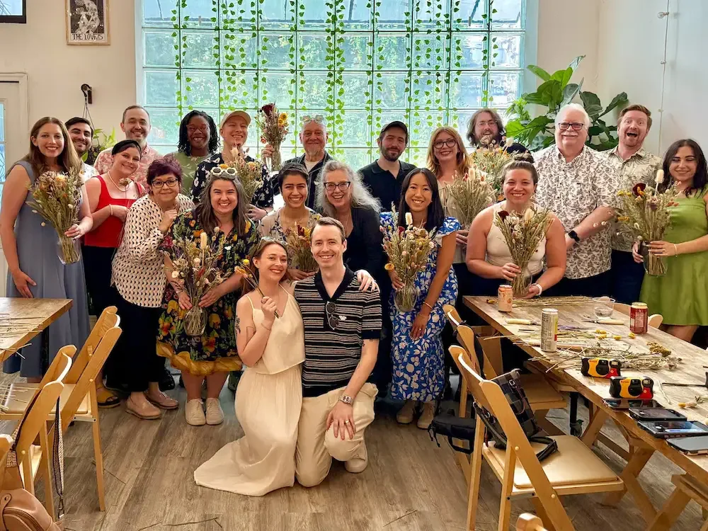 A large smiling group holding dried-flower bouquets at a private party at Bat Haus, a small party venue in Williamsburg, Brooklyn.