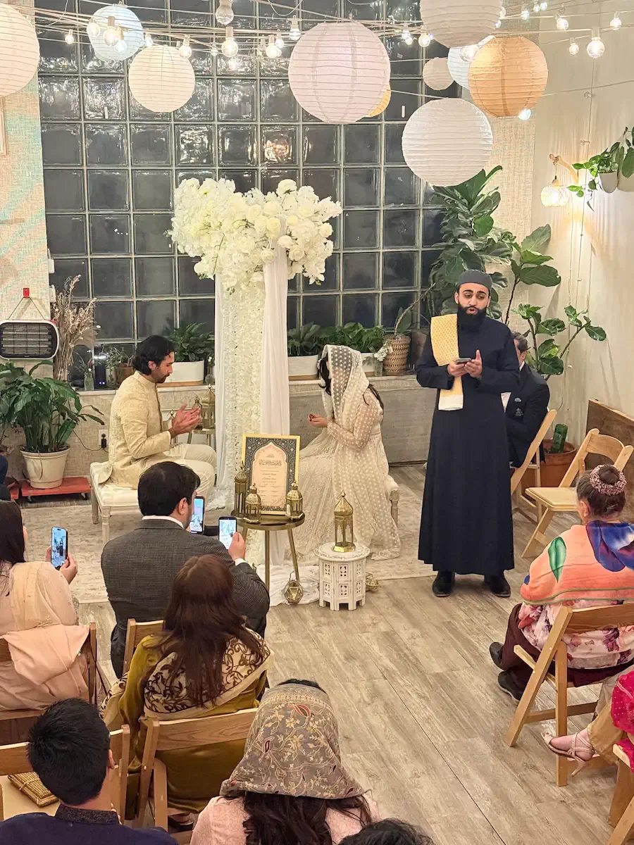 A Nikah ceremony with a white floral arch in front of the glass-block window at Bat Haus event space in Brooklyn.