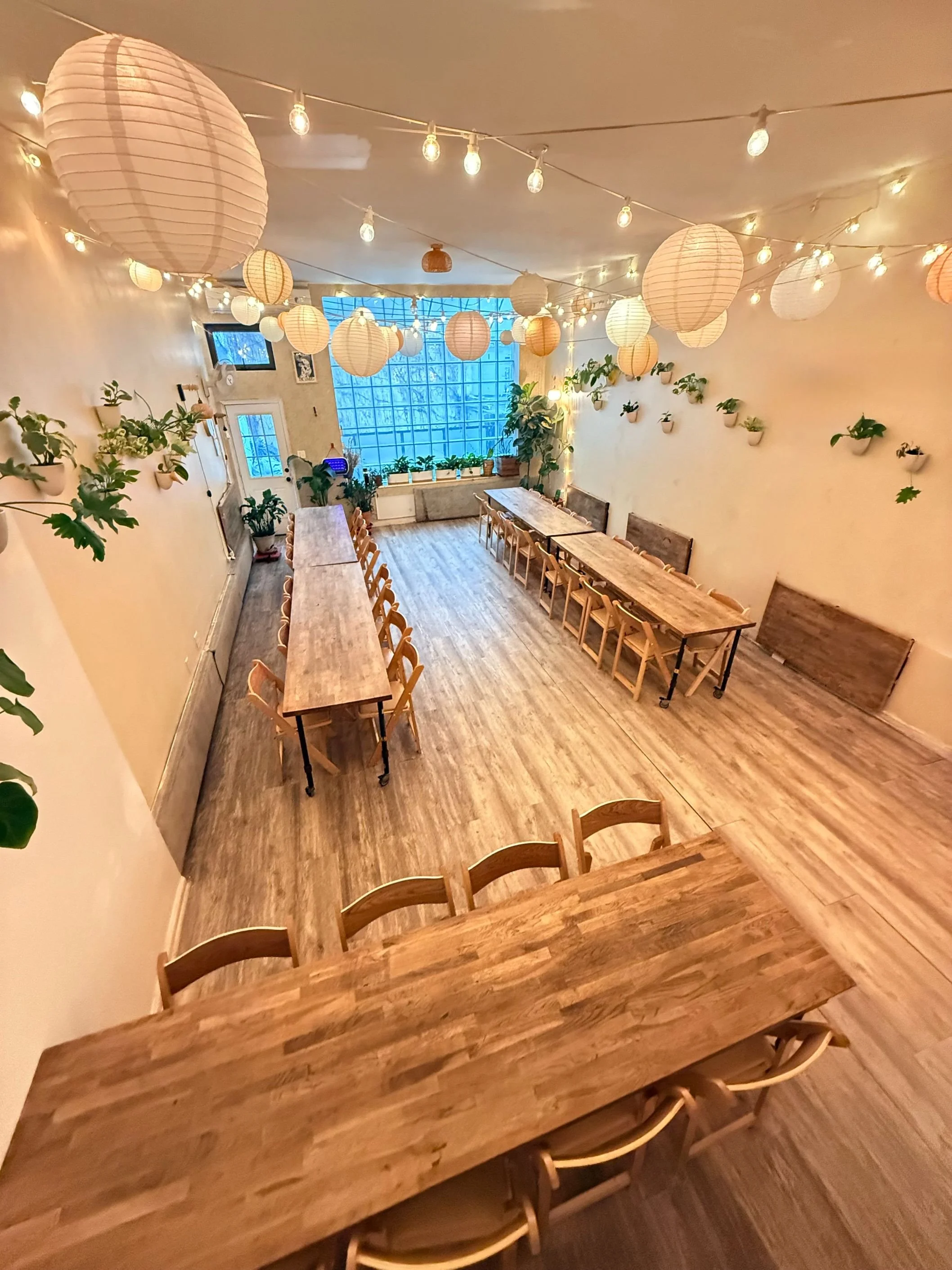 Bat Haus event space in Williamsburg Brooklyn set with long wooden tables, folding chairs, string lights, and plants, included amenities for private party rentals up to 50 guests.