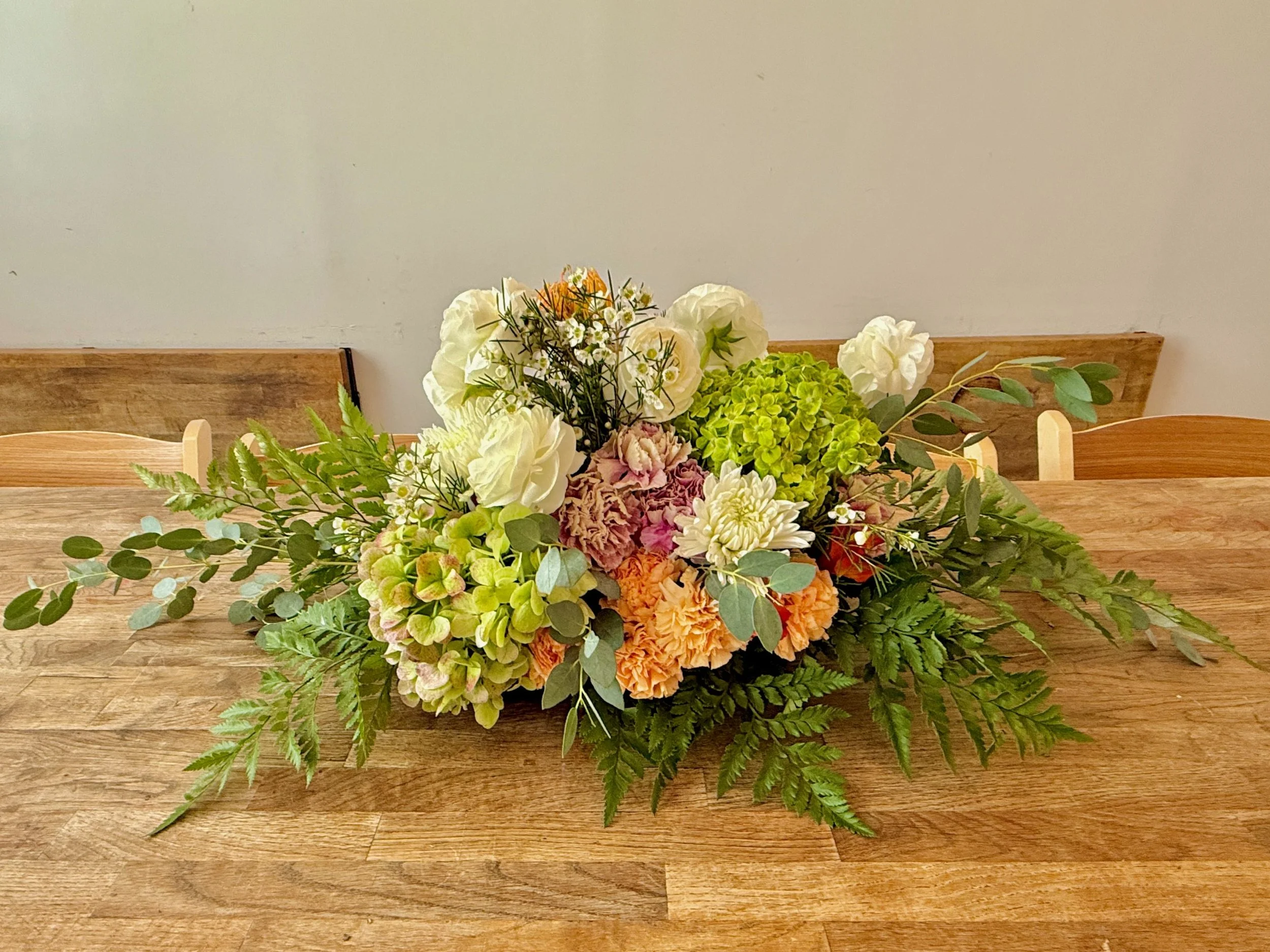 Soft Garden — Blush, Cream & Green
A romantic take with blush ruffles, cream blooms, and layered greens. Eucalyptus and fern create a gentle taper at both ends—perfect for family-style tables.
Vibe: soft, textured, timeless.