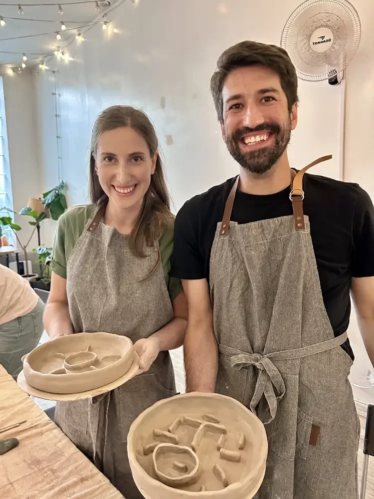 Corporate team members wearing aprons during a hand-building pottery class at Bat Haus in Brooklyn, holding freshly made clay pieces during a creative team building workshop.