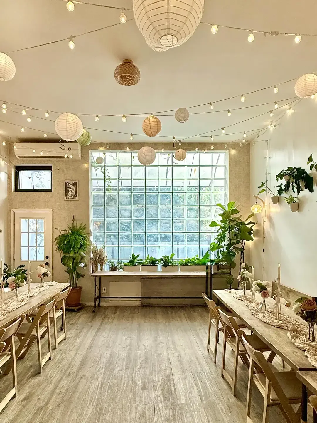 Brooklyn event venue at Bat Haus in Williamsburg with glass block window wall, string lights, paper lanterns, long wooden tables, and plants set for a private celebration or wedding dinner