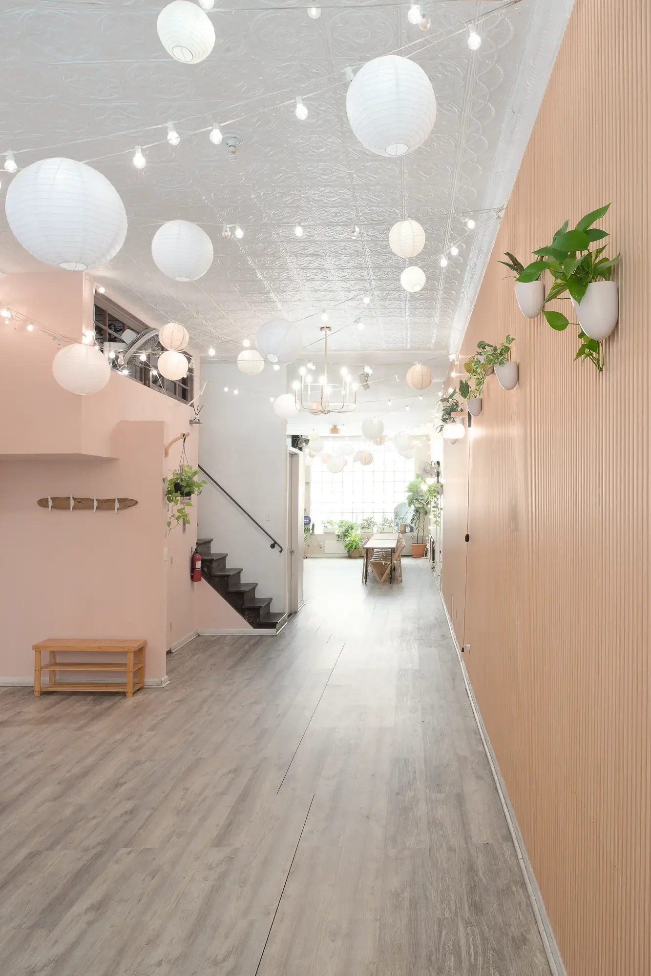 View through Bat Haus event space in Williamsburg, Brooklyn, showing the staircase to the downstairs studio, warm string lights, and tin ceilings