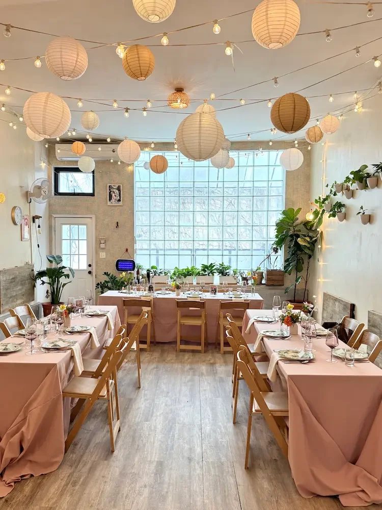 Light filled Brooklyn event space at Bat Haus in Williamsburg with long wooden tables, blush linens, and warm string lights, set up for an intimate gathering
