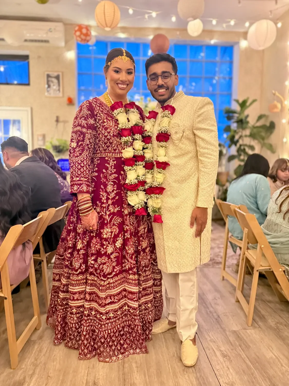 Bride in a red embroidered outfit and groom in cream with flower garlands at their nikkah at Bat Haus in Brooklyn