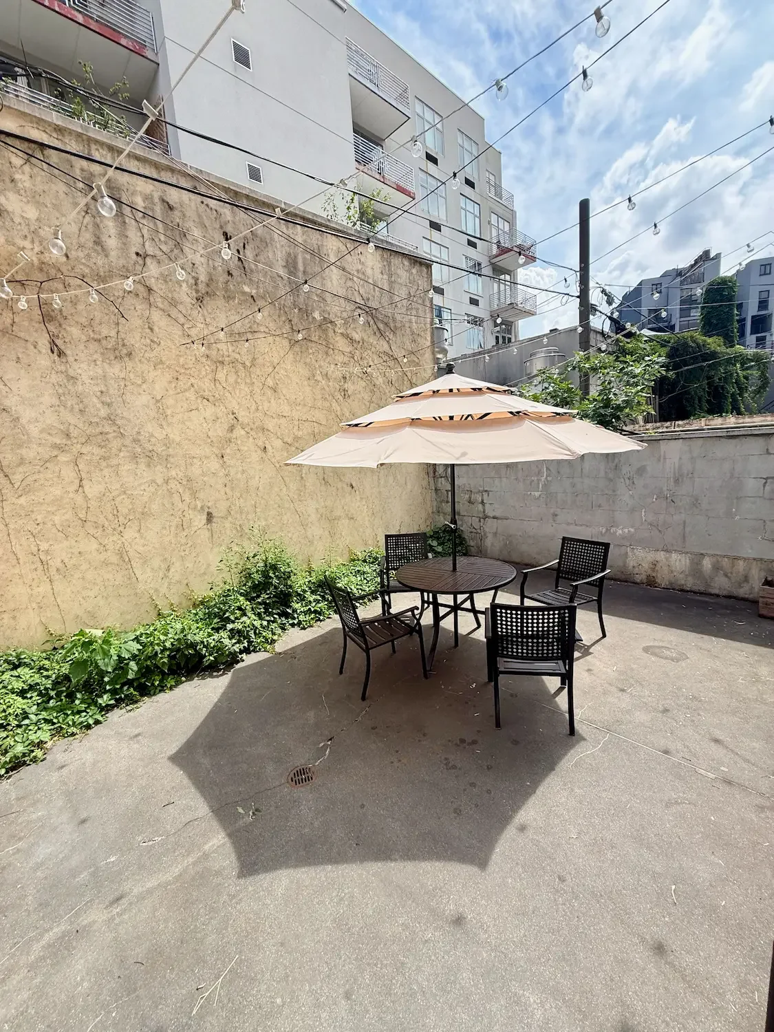 Private backyard patio at Bat Haus with string lights, umbrella-shaded seating, and brick walls - the outdoor space for baby showers in Williamsburg, Brooklyn."