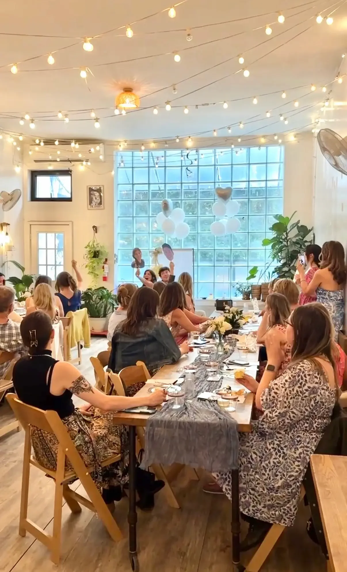 Bridal shower celebration at Bat Haus in Brooklyn with guests seated at long wooden tables under string lights and glass block windows.