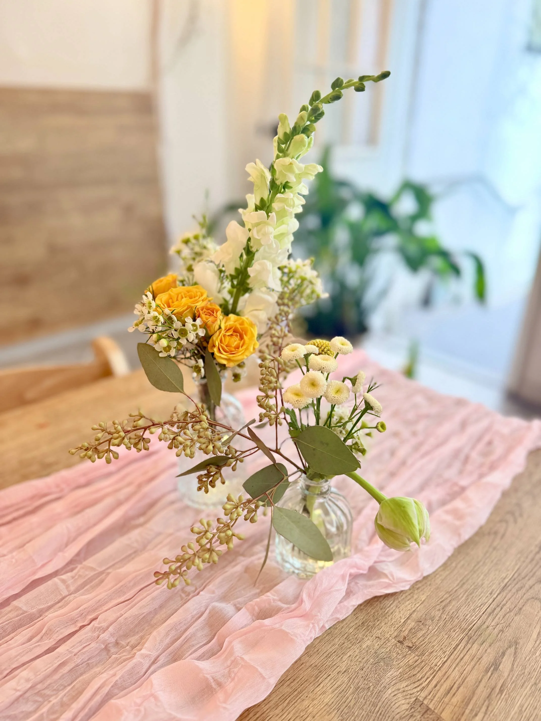 Bud vase floral arrangement from the Bat Haus Styled Package featuring soft yellow and white blooms, greenery, and an airy, romantic table styling.
