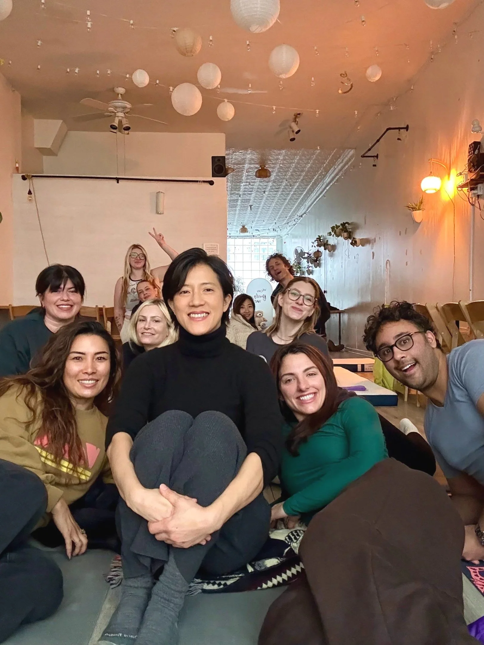Group of participants smiling together after a sound bath experience at Bat Haus in Brooklyn, seated on yoga mats in a warm, light filled studio.