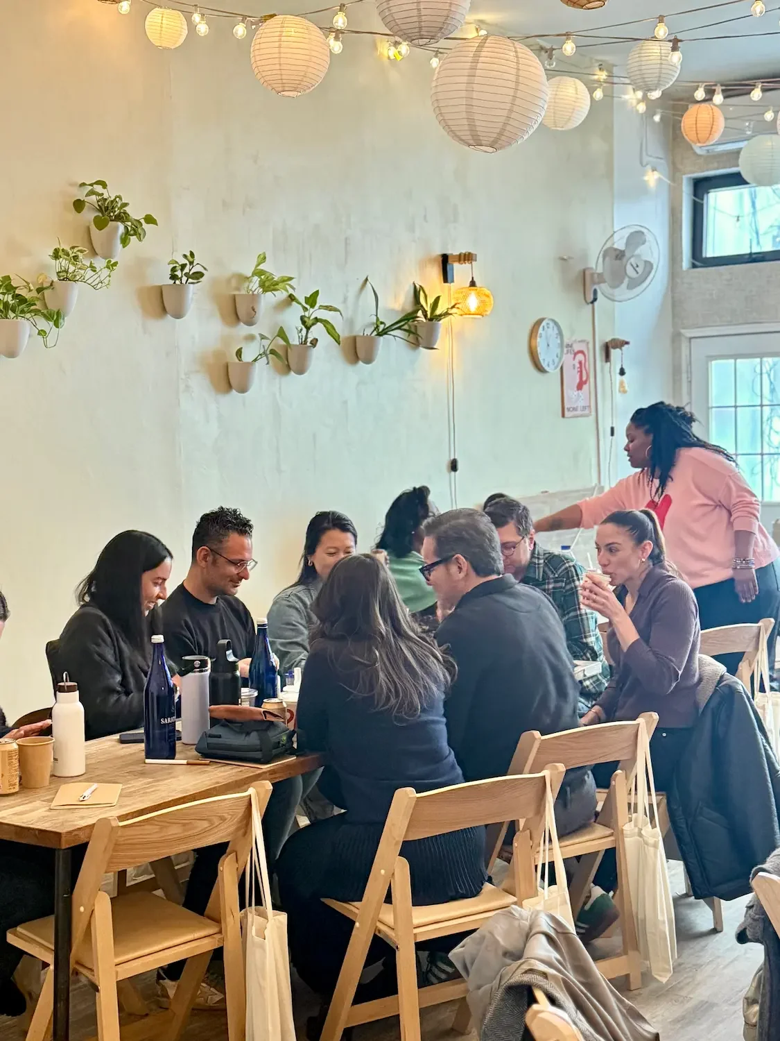 Davines team seated at long wooden tables during a corporate offsite at Bat Haus in Brooklyn with warm string lights and indoor plants