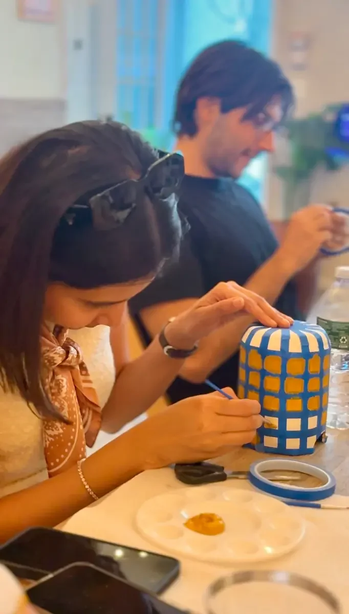 A guest painting a blue and mustard grid pattern onto a ceramic lamp base.