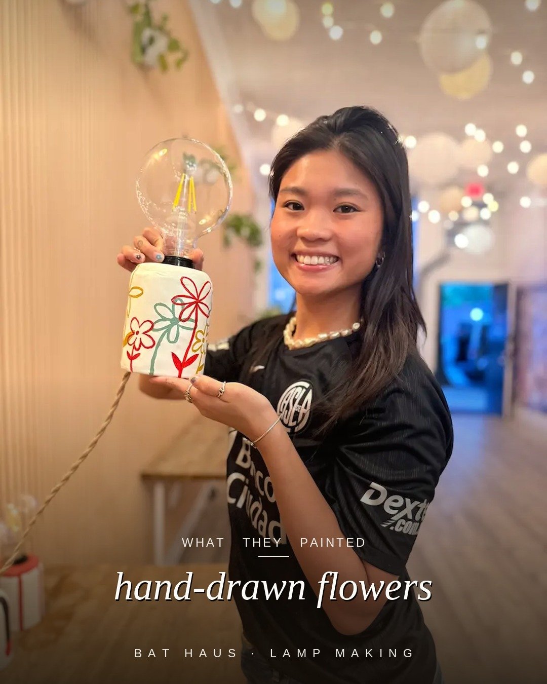 Workshop guest holding a handmade lamp painted with colorful hand-drawn flowers.
