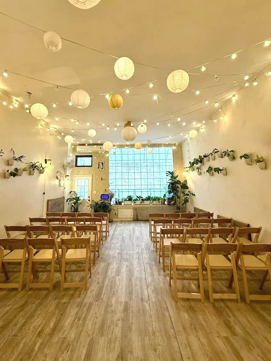 Ceremony style seating layout at Bat Haus Brooklyn event space with rows of chairs facing the window wall under string lights and lanterns.