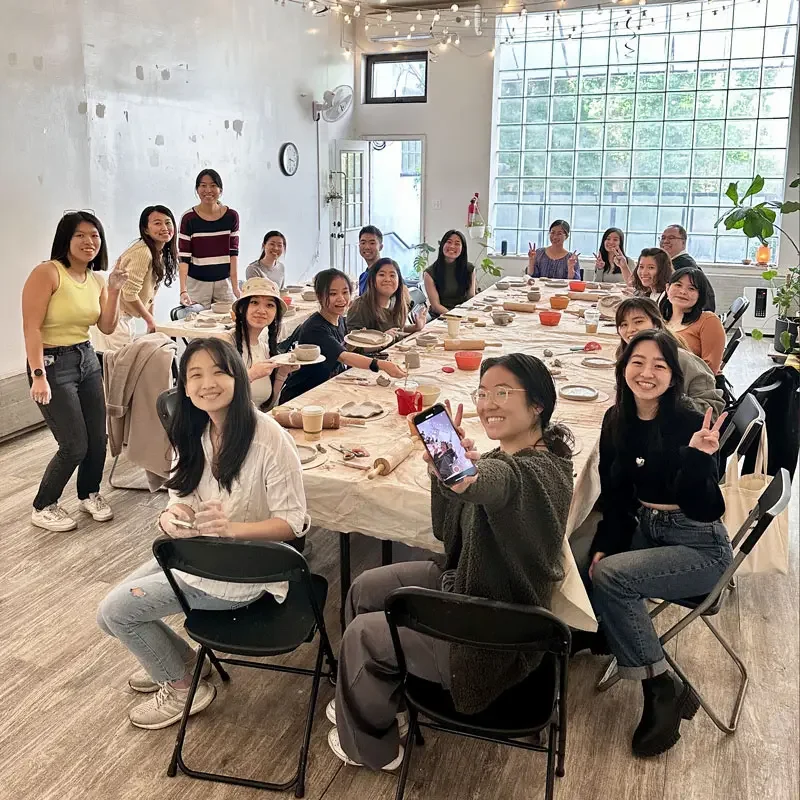 Private group pottery class at Bat Haus in Brooklyn with participants seated around long tables hand building ceramic pieces in a bright studio