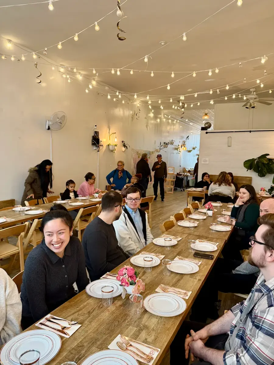 Graduation party celebration at Bat Haus in Brooklyn with guests seated at long wooden tables under string lights in a bright, airy event space.