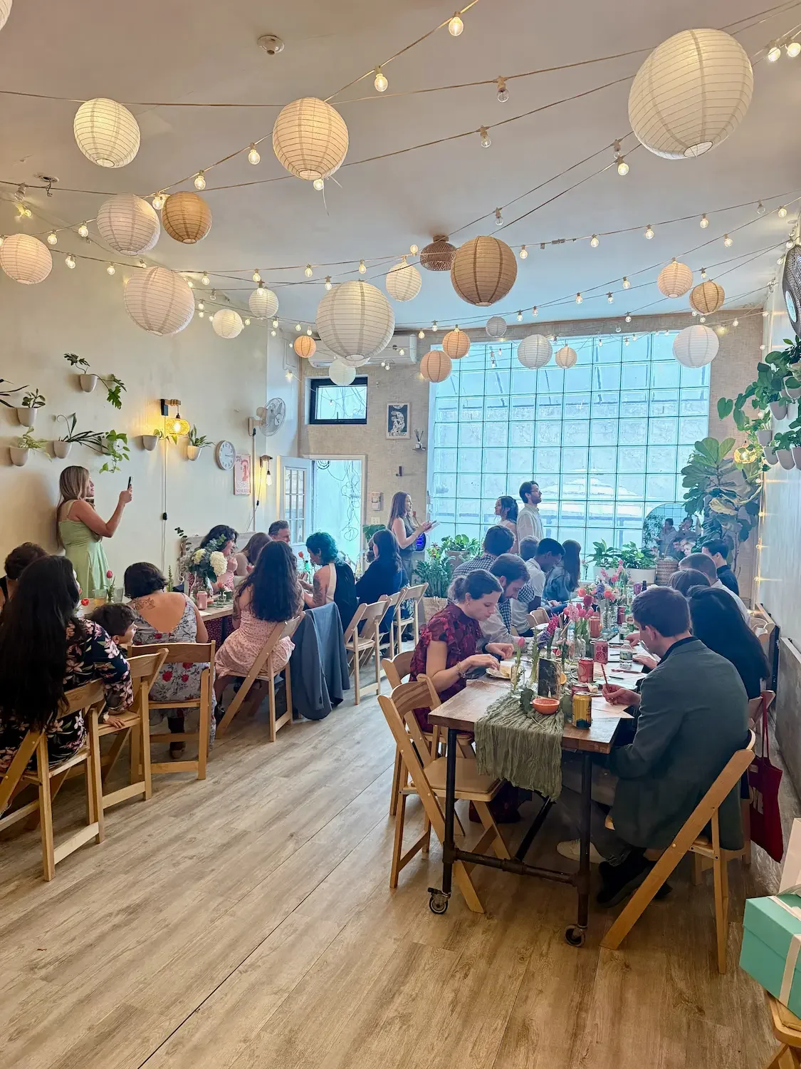 Guests seated at a long table under string lights and lanterns at an engagement party at Bat Haus in Williamsburg, Brooklyn.
